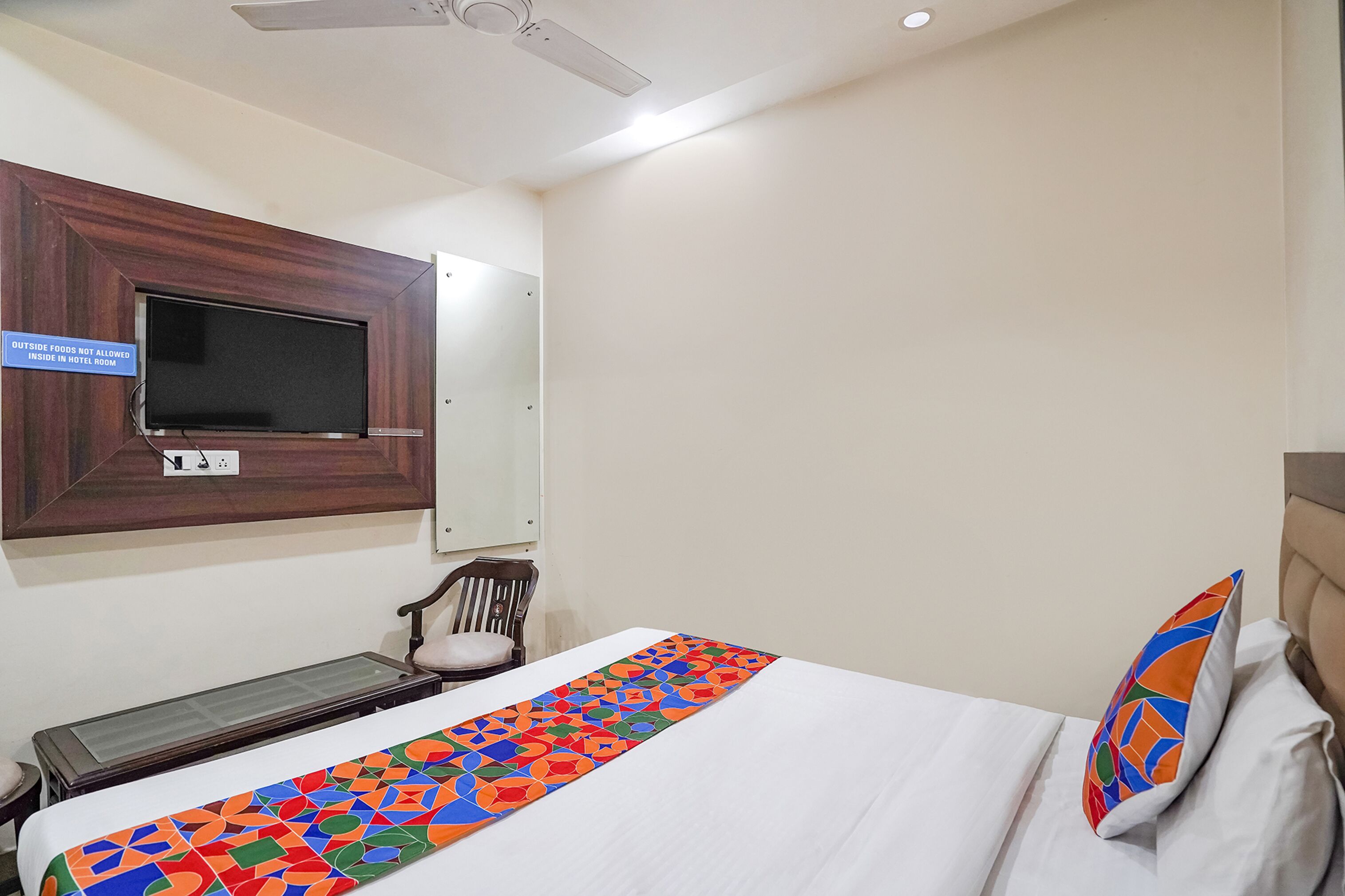 A hotel room with a bed, a TV mounted on the wall, a desk, and a chair.