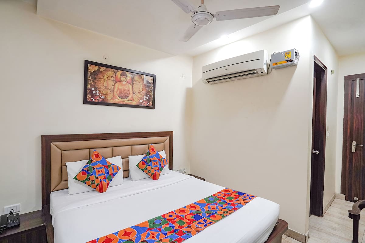 Habitación de hotel con cama, ventilador de techo, aire acondicionado, puerta y un cuadro colgado en la pared.