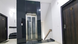 Een moderne lift met een digitaal scherm, een donker houten deur met nummerplaat en een trap met een leuning.