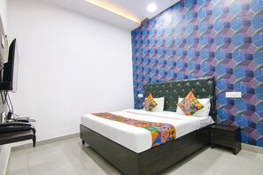 Une chambre moderne avec un grand lit, une tête de lit verte recouverte de tissu et un mur orné d’un motif.