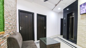 Een hal met twee donkerhouten deuren met de aanduiding '101', een tafel met glazen blad, een grijze bank en een muur met een bakstenen patroon en groen kunstgras.