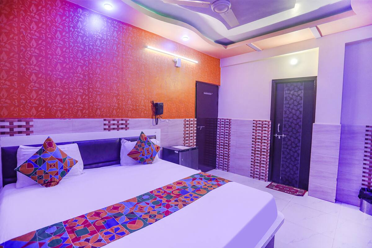 A hotel room with a large bed, a headboard, a bedside table, a nightstand, a wall-mounted phone, a door, and a patterned wall.