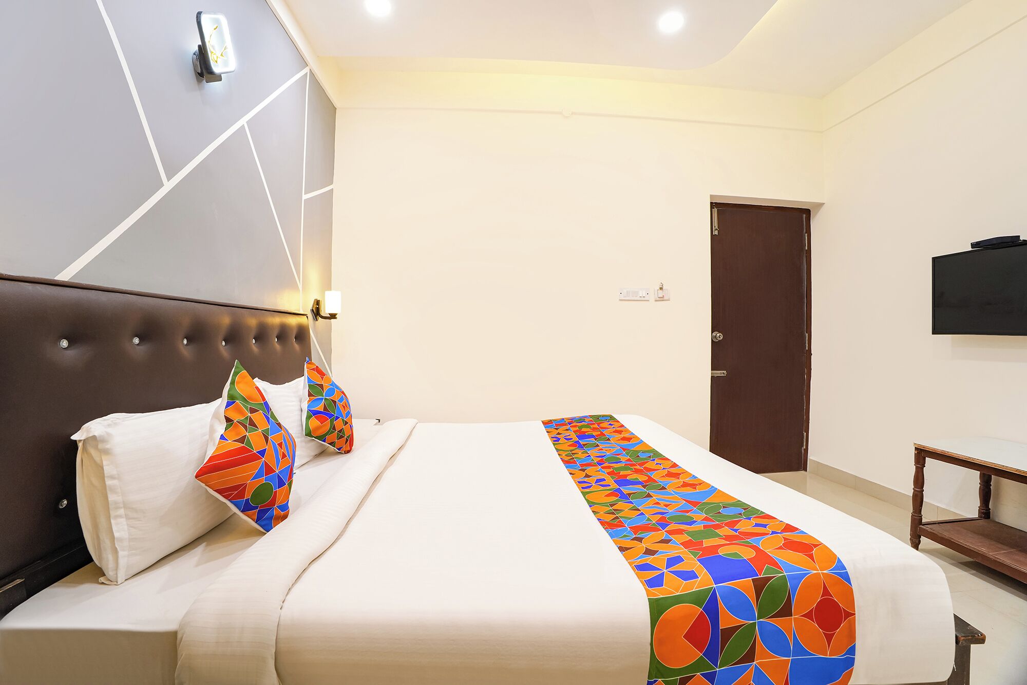 Une chambre d’hôtel avec un lit, une tête de lit, un téléviseur fixé au mur et une porte.