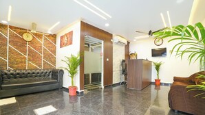 Un vestíbulo con un sofá de cuero negro, dos plantas en macetas, un mostrador de recepción y un reloj en la pared.