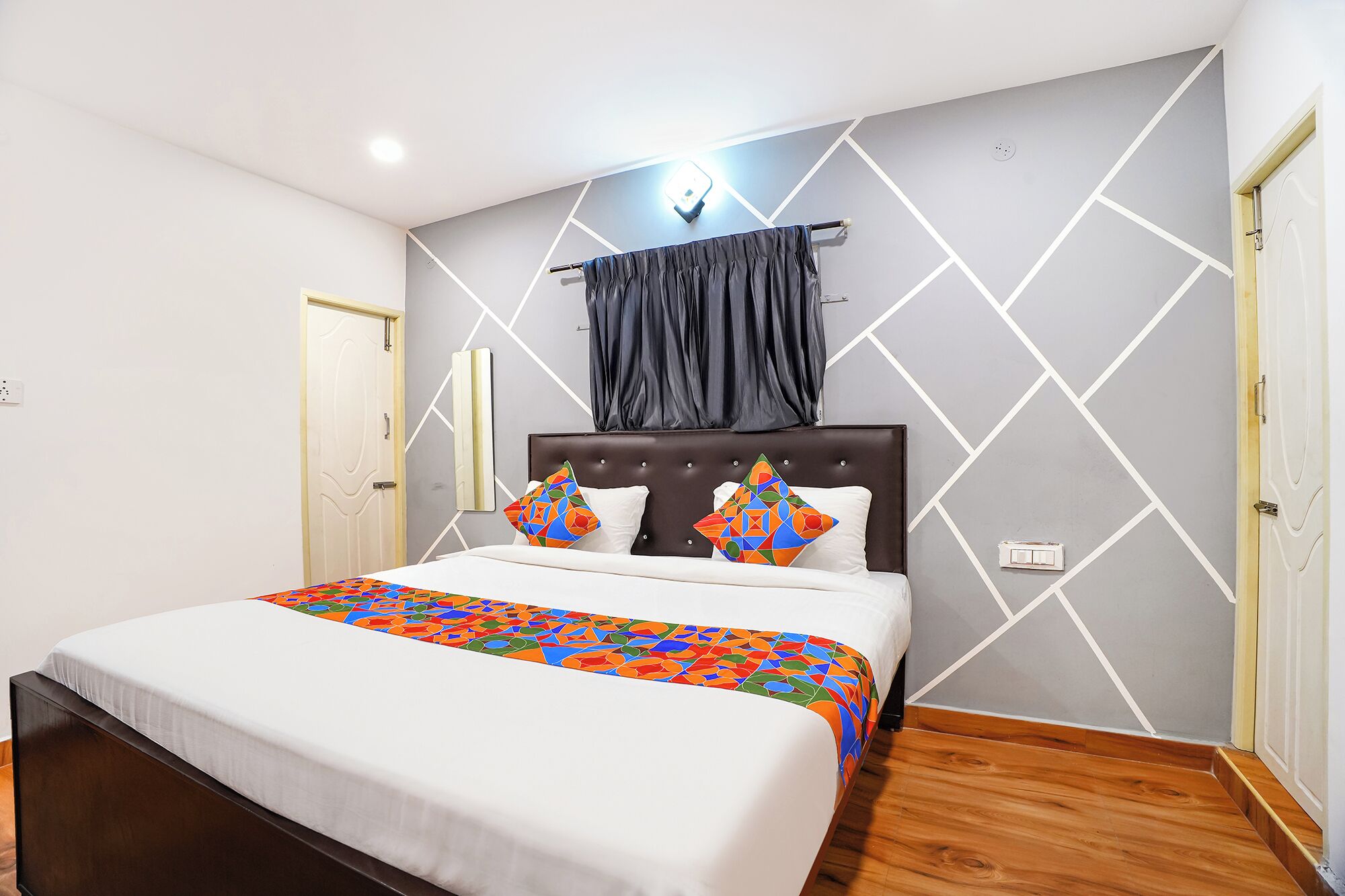A modern bedroom with a bed, a headboard, a wall-mounted light, and a geometric-patterned wall.