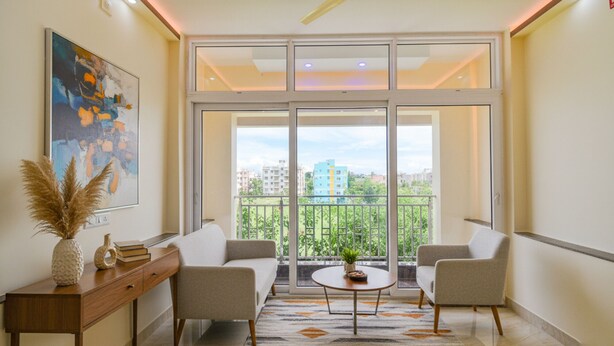 A modern living room with a sofa, two armchairs, a coffee table, and a large window with a view of buildings and greenery.