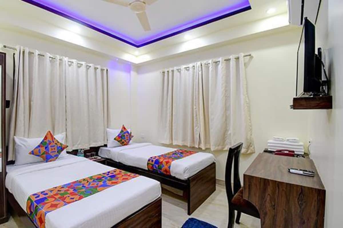 A hotel room with two beds, a desk, a chair, and a TV.