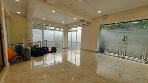 A spacious lobby with a polished marble floor, several pieces of luggage, and a large window offering a view of greenery outside.