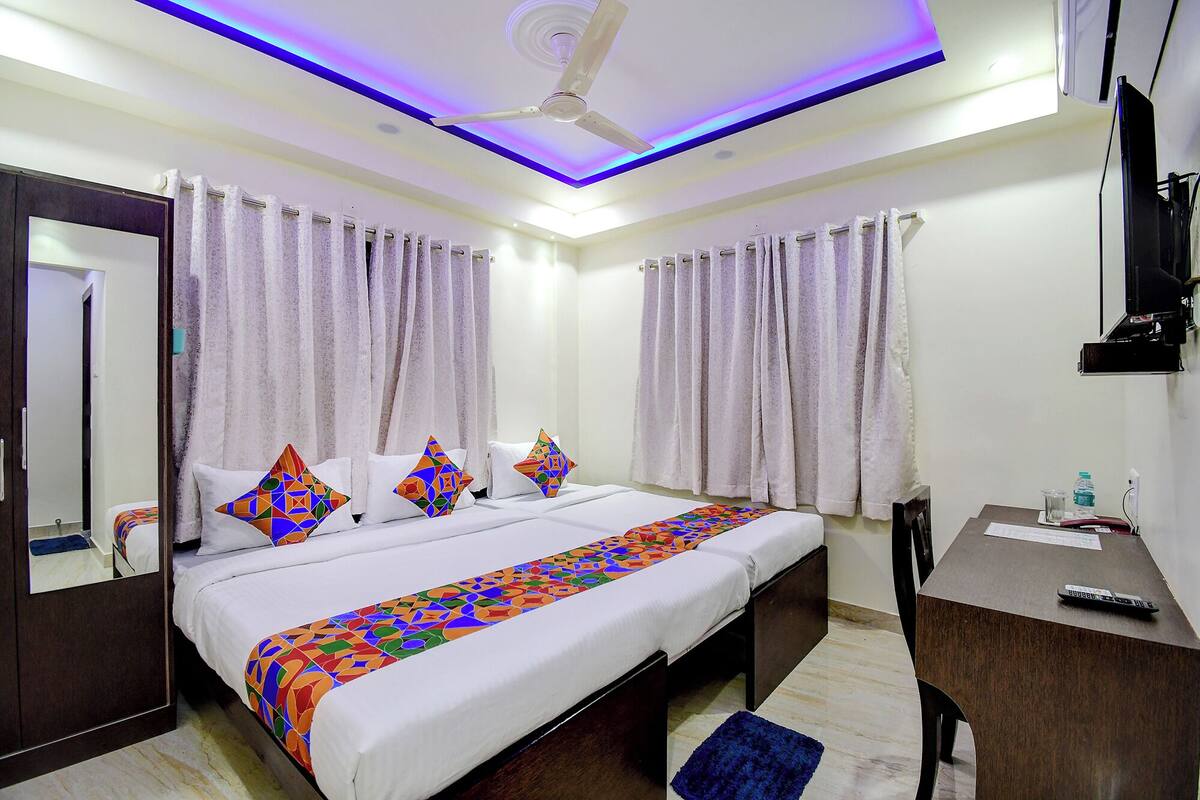 A hotel room with a bed, a desk, a chair, a ceiling fan, and curtains.
