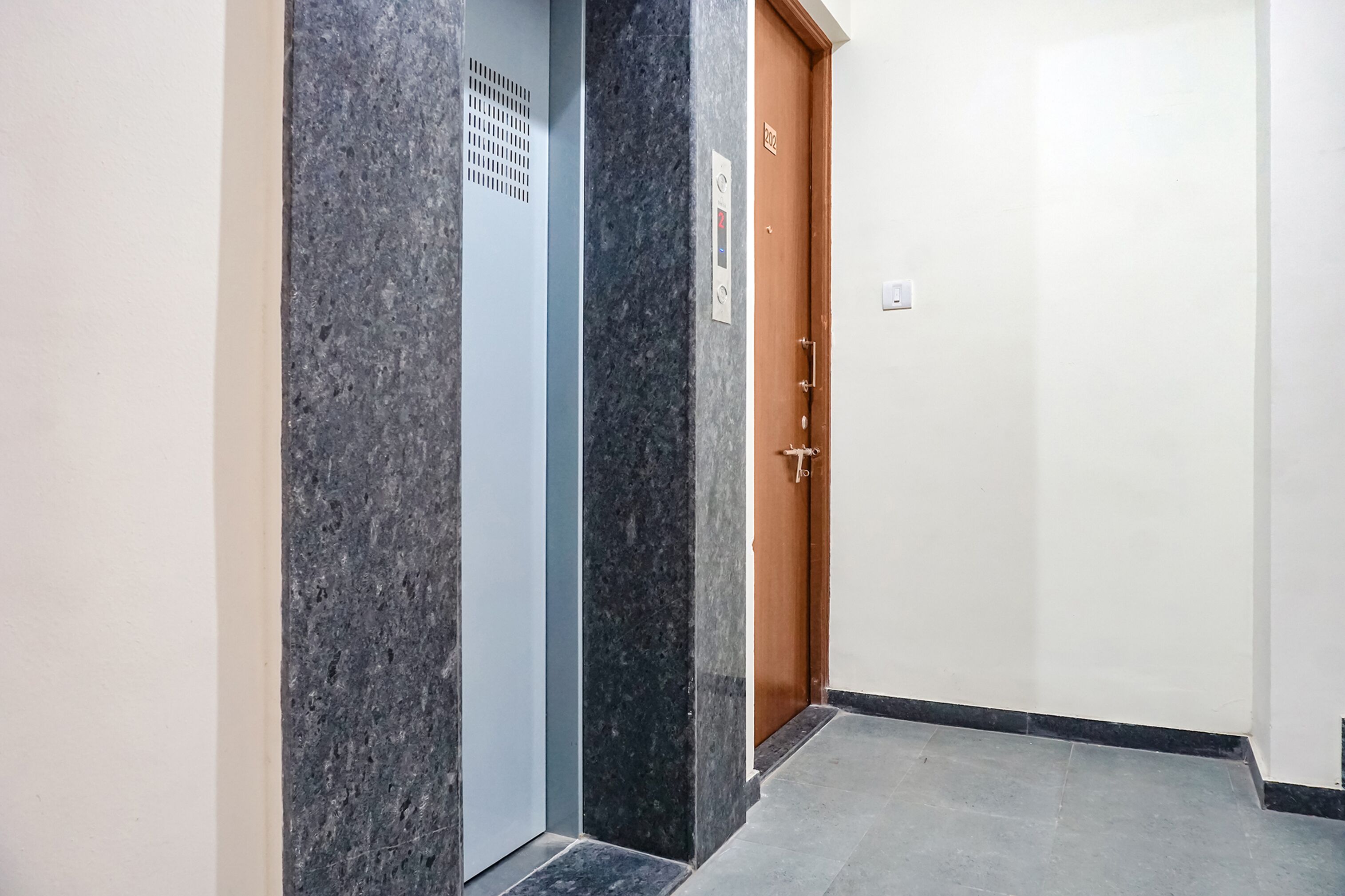Un pasillo con pared de mármol, un ascensor azul y una puerta de madera con un letrero.