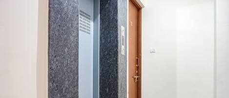 A hallway with a marble wall, a blue elevator, and a wooden door with a sign.