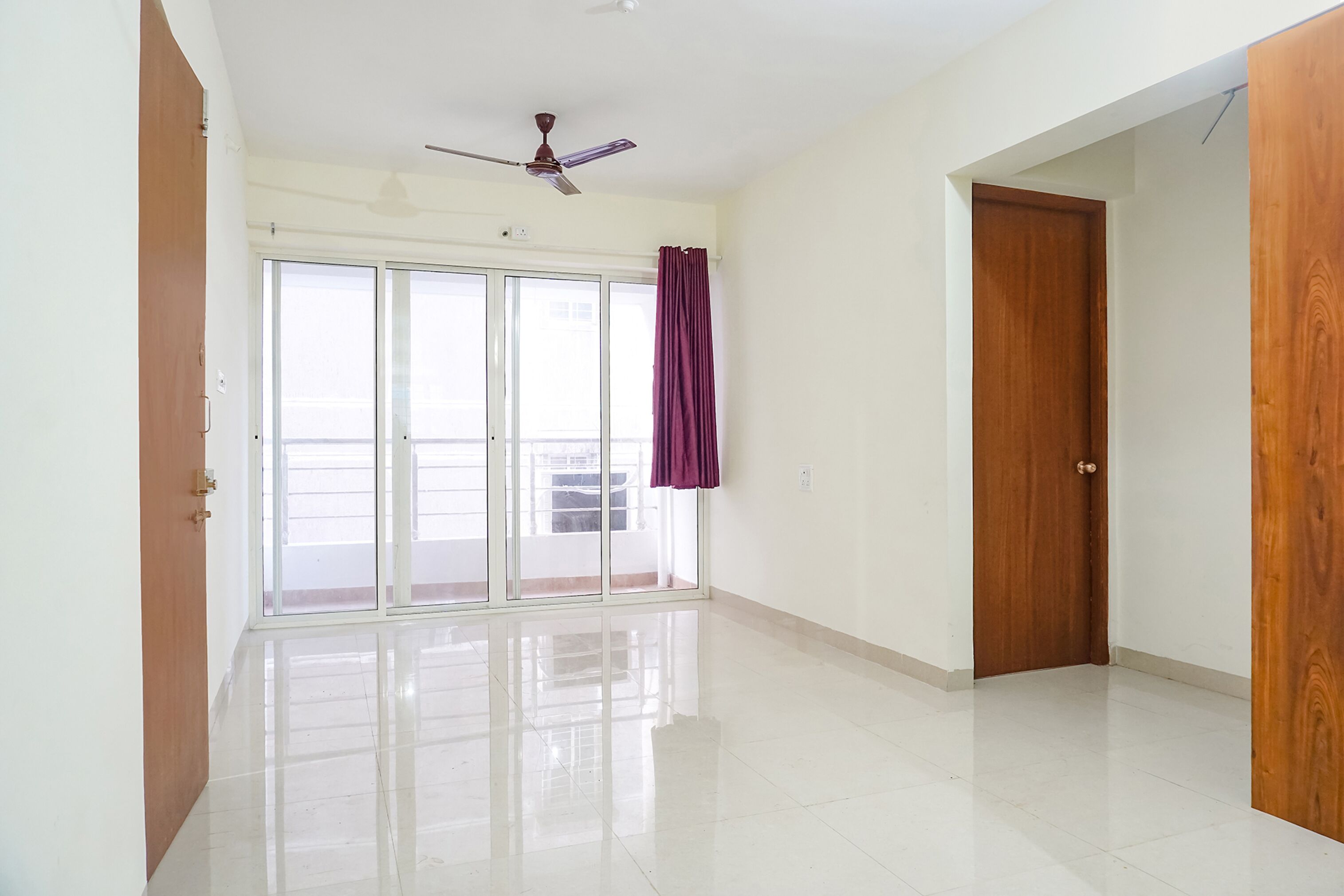 A spacious room with a large sliding glass door leading to a balcony, a ceiling fan, and a wooden door.