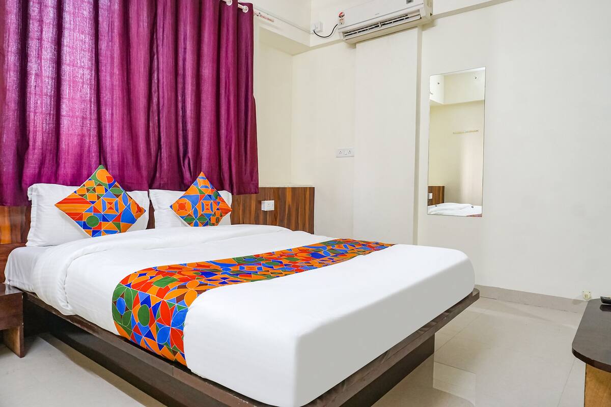 A hotel room with a bed, a wooden headboard, a mirror, and a window with curtains.