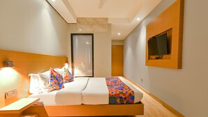 A modern bedroom with a wooden headboard, a bed with colorful bedding, a bedside table, and a mounted TV on the wall. - FabHotel Penthouse (Guwahati)
