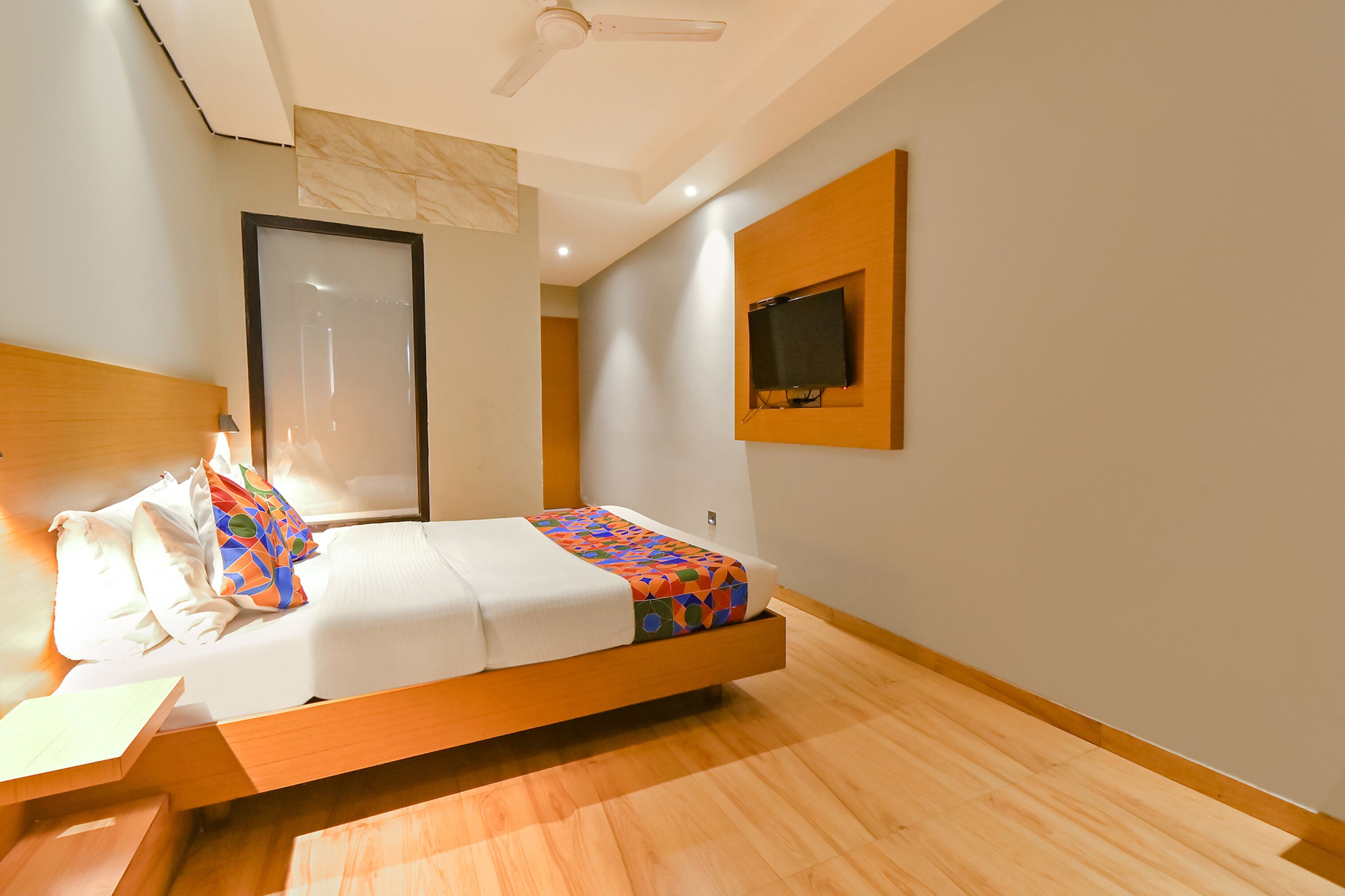 Una habitación de hotel moderna con una cama de madera, un televisor de pantalla plana montado en la pared y un ventilador de techo.