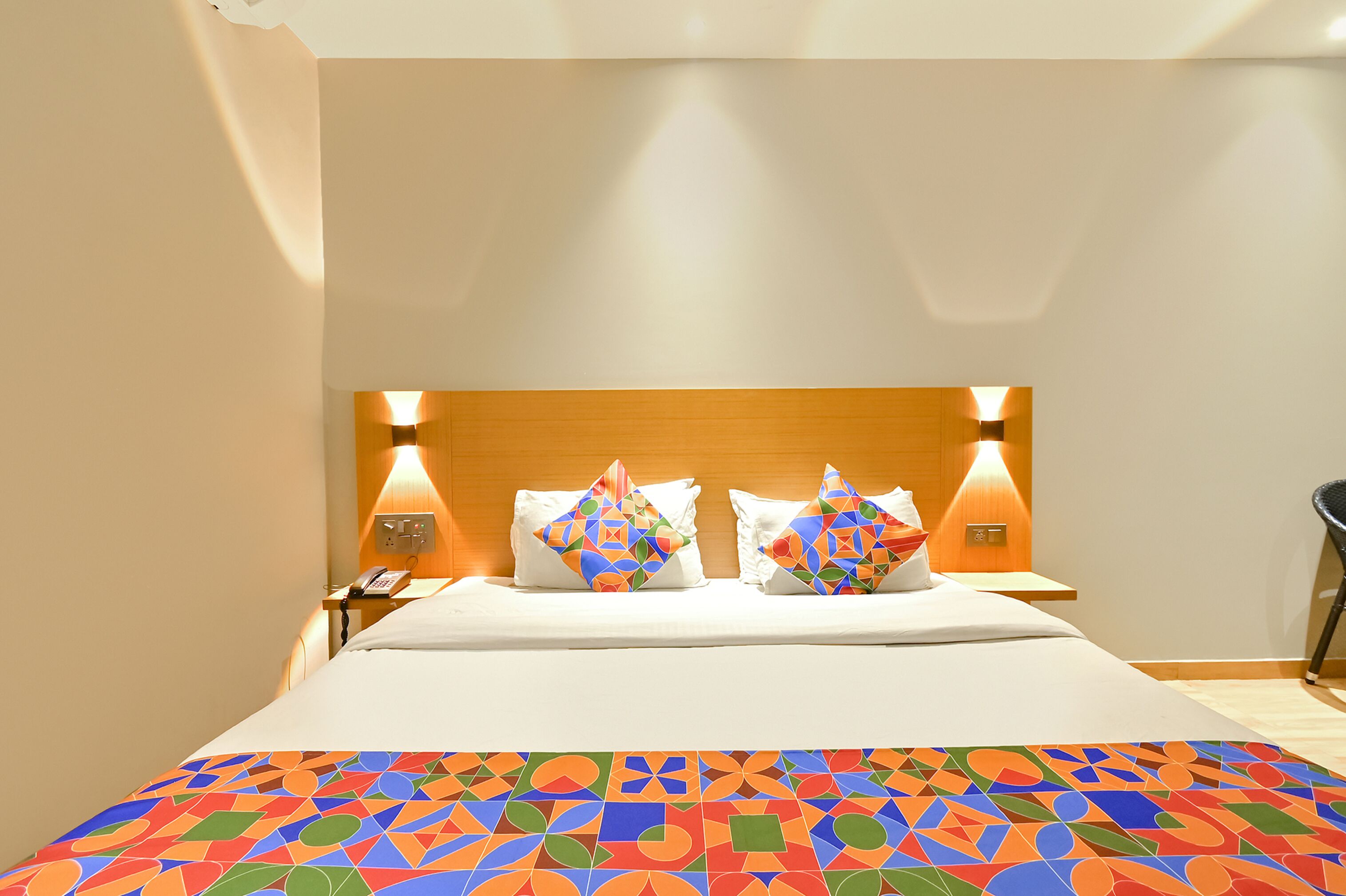 A hotel room with a wooden headboard, two bedside lamps, a telephone, and a colorful bedspread.