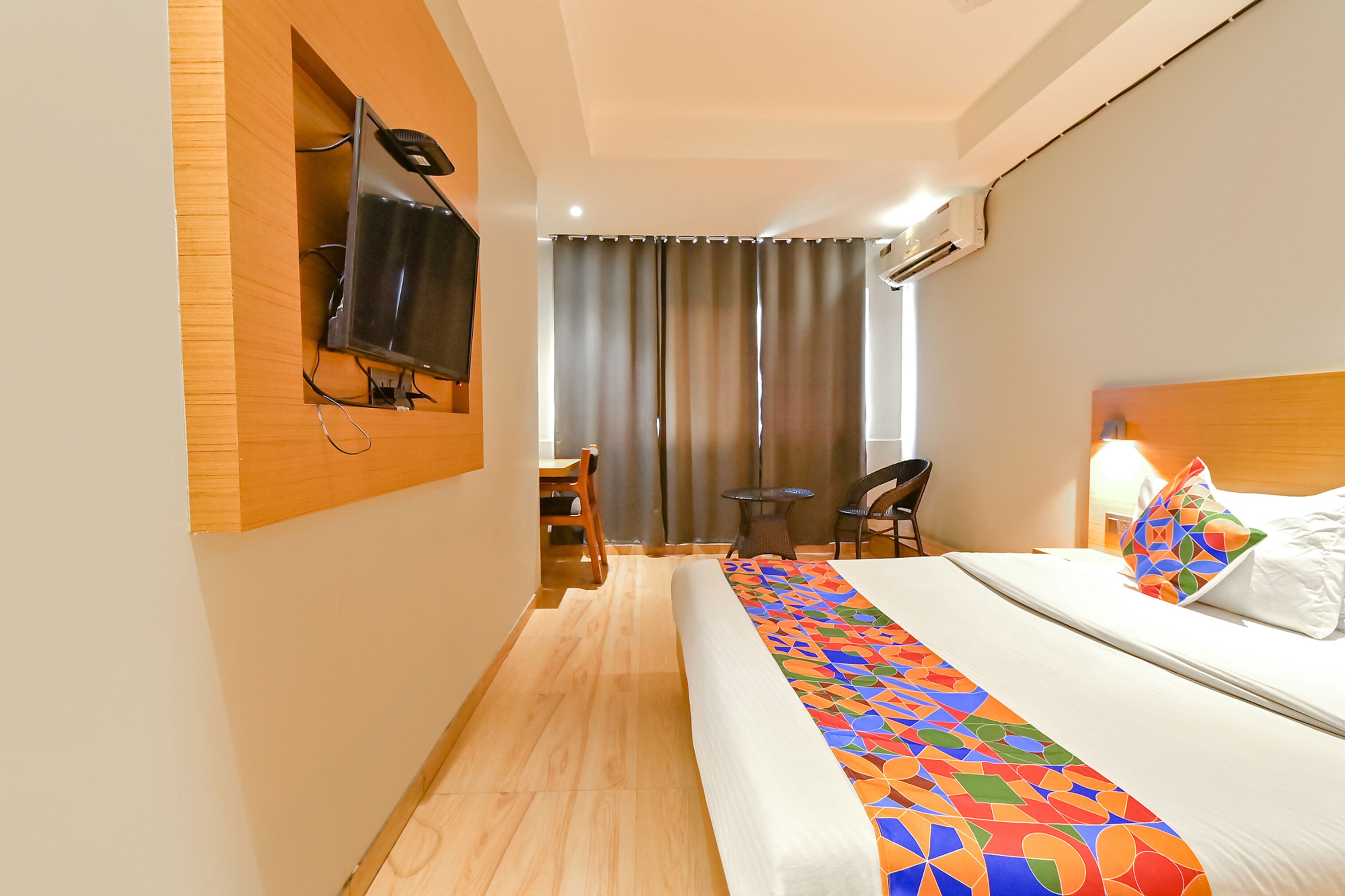 A hotel room with a bed, a TV mounted on the wall, a desk, and a chair.
