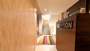 A reception area with a wooden floor, a reception desk, and a staircase in the background. - FabHotel Penthouse (Guwahati)