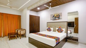 A hotel room with a bed, a desk, a chair, a wardrobe, a ceiling fan, and a mirror. - Fabhotel Swaraj (Palghar)