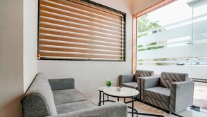 A modern lounge area with grey sofas, a small round table, and a large window with blinds. - Fabhotel Swaraj (Palghar)