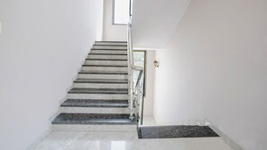 A modern staircase with marble steps and a glass railing, leading to a landing with a door and a small window. - Fabhotel Swaraj (Palghar)