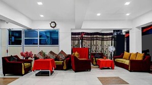 A spacious living room with red sofas, a dining table, and a large window with curtains. - Fabhotel Prime Finesse (Pune)