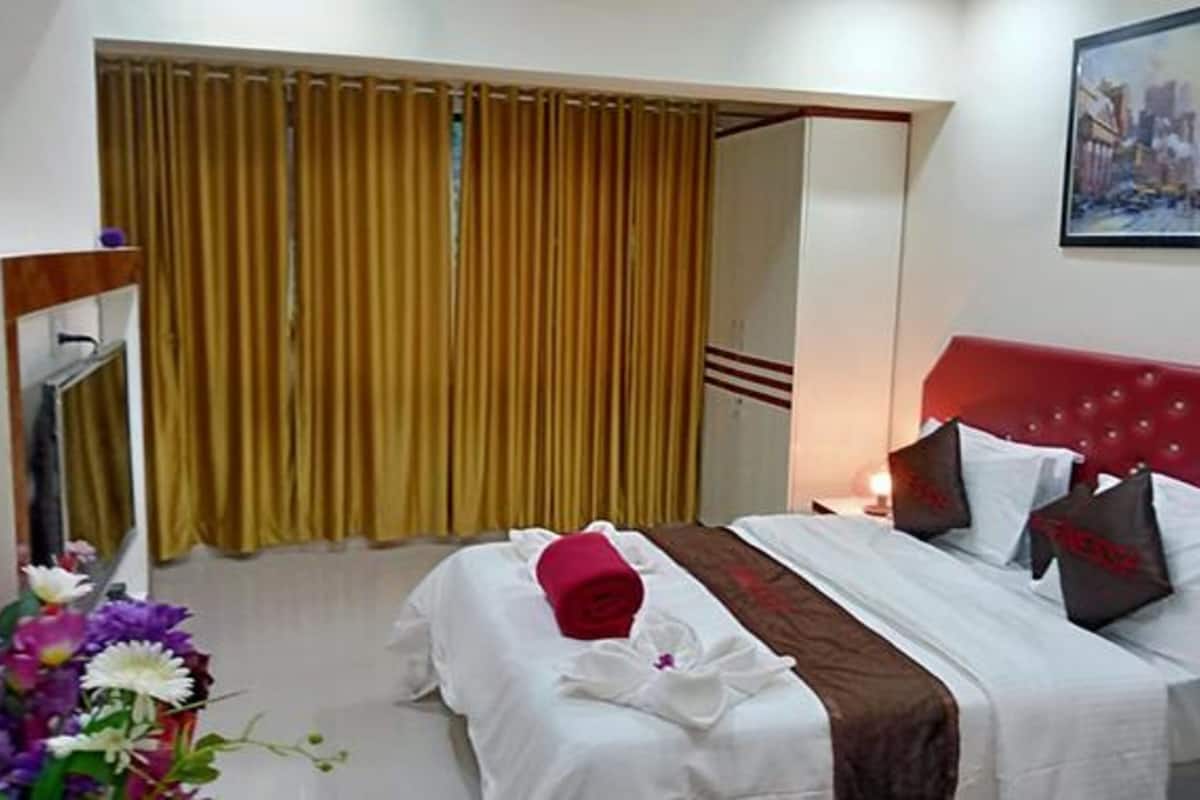Quarto de hotel com cama, cortinas, um quadro e um vaso de flores.