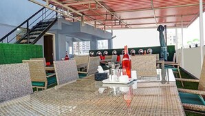 An outdoor seating area with wicker furniture, a glass table, and a red bottle. - Fabhotel Prime Finesse (Pune)