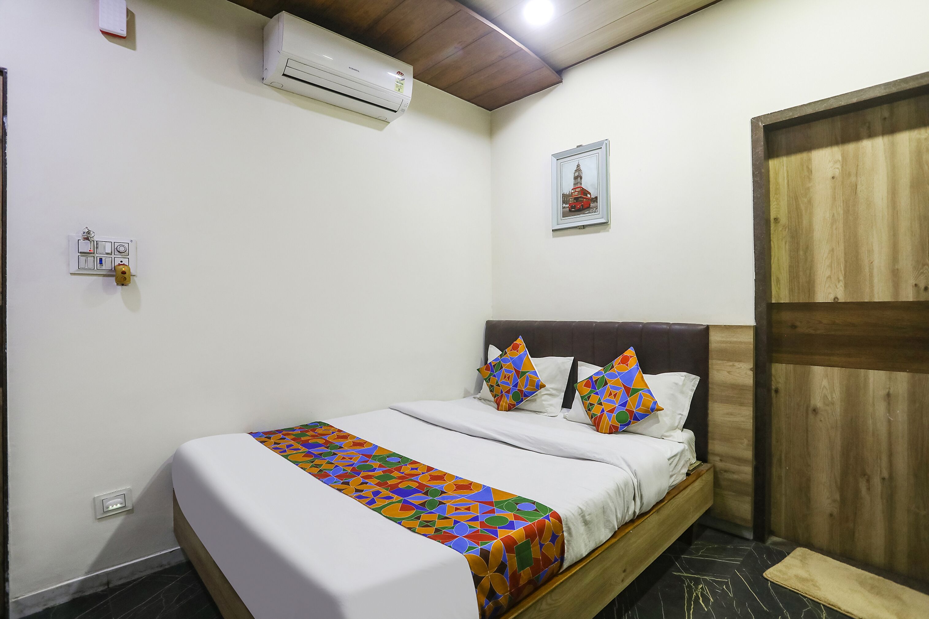 A neatly made bed with a colorful geometric-patterned bedspread, a wooden headboard, and a small wooden bench beside the bed.