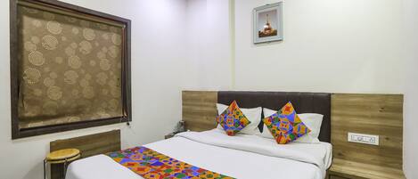 A neatly arranged hotel room with a bed, a small stool, a nightstand, and a wall-mounted picture.