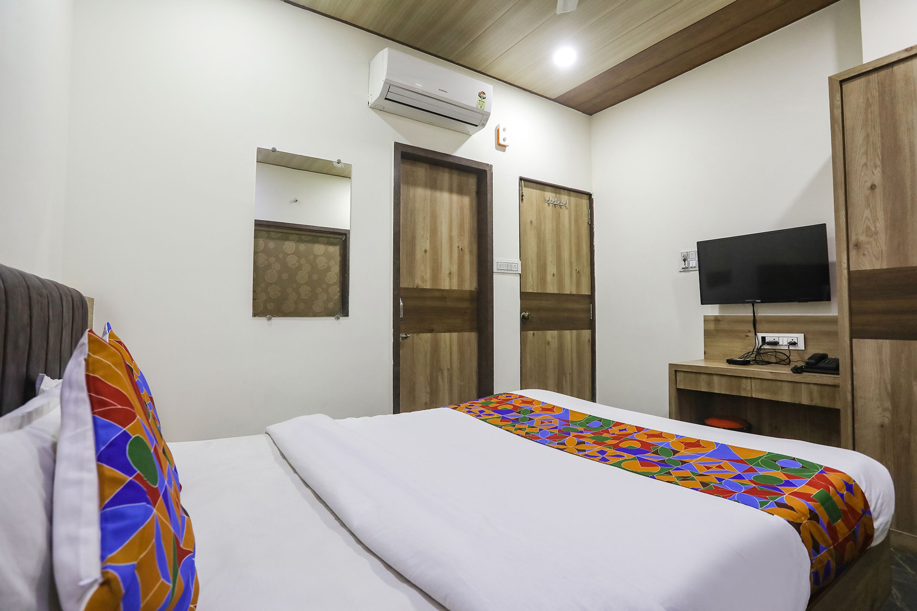 A hotel room with a bed, a TV, a wardrobe, and an air conditioning unit.