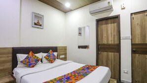 A neatly made bed with a colorful geometric throw, a wooden headboard, and a wall-mounted air conditioner. - Fabhotel Vedanta Inn (Nagpur)