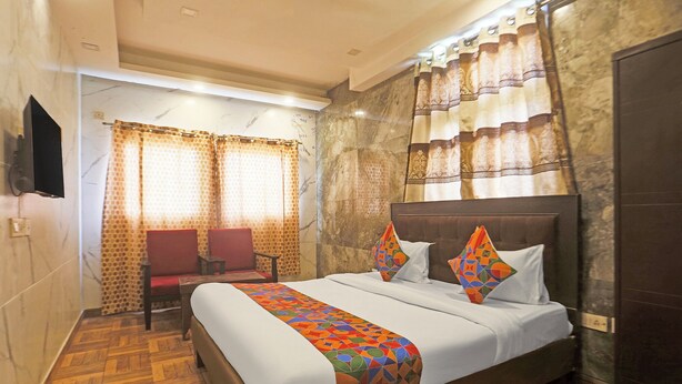 A hotel room with a large bed, a television mounted on the wall, a seating area with two chairs, and a patterned curtain. - FabHotel Trish The Gera (New Delhi)