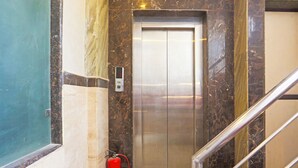An elevator with a digital display, a fire extinguisher, and a marble wall. - FabHotel Trish The Gera (New Delhi)