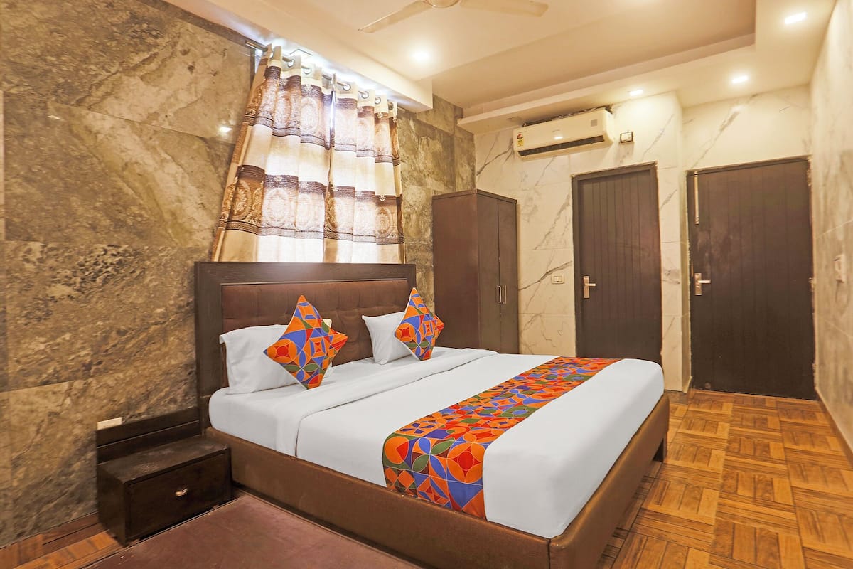 A hotel room with a marble wall, a bed with a patterned bedspread, a nightstand, a wardrobe, and a wooden floor.
