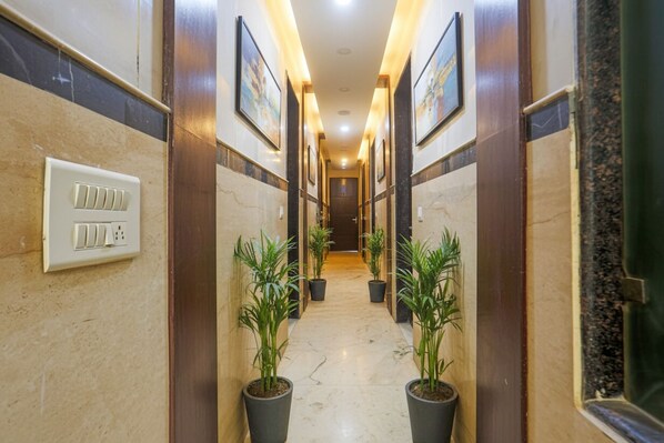 A hotel hallway with marble walls, potted plants, and framed artwork on the walls. - FabHotel Trish The Gera (New Delhi)