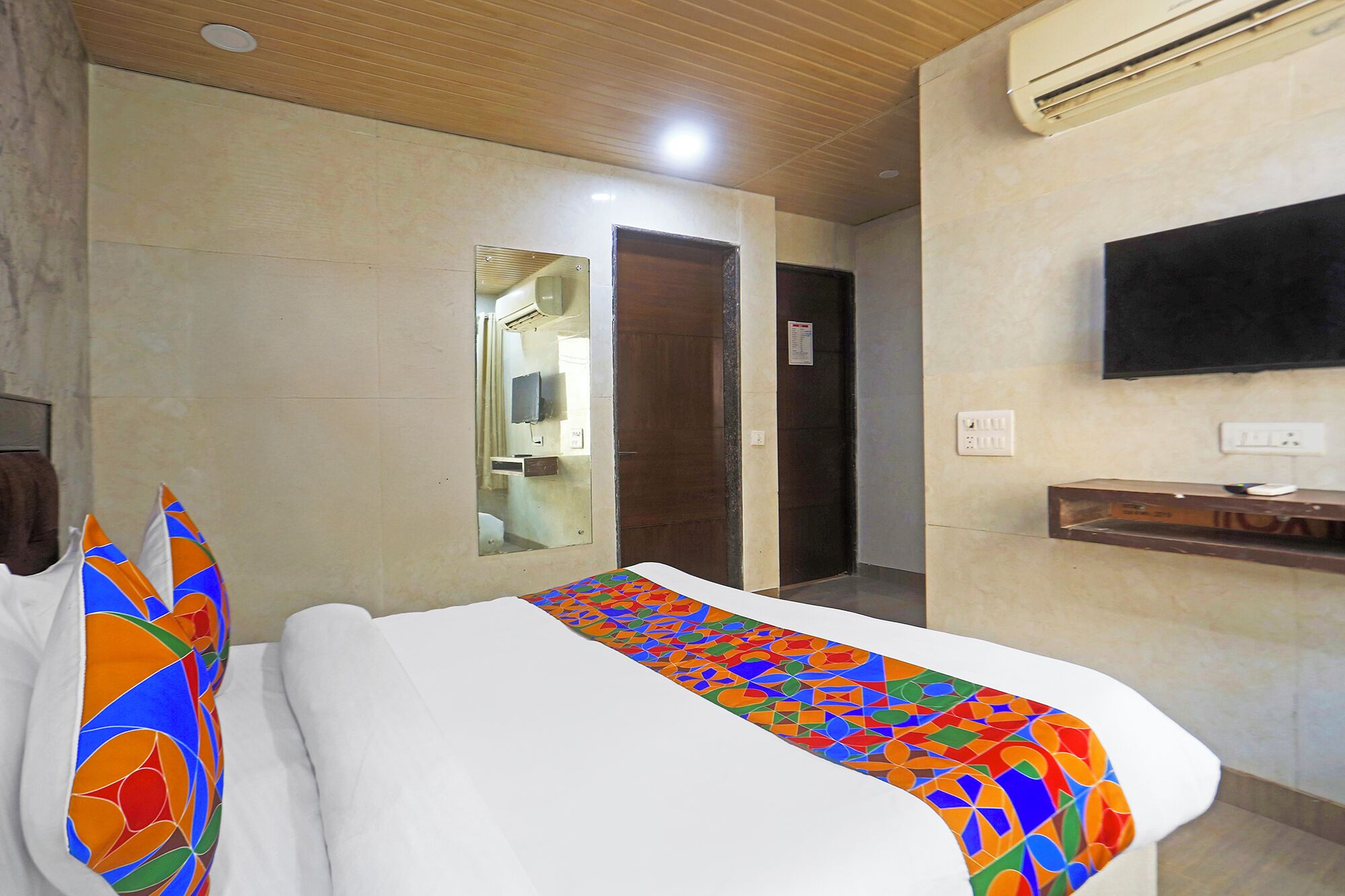 Habitación de hotel con cama, televisión montada en la pared y baño visible a través de un espejo.