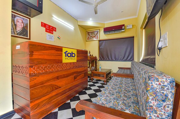 A hotel room with a checkered floor, a wooden reception desk, a sofa with a patterned cover, and a ceiling fan.