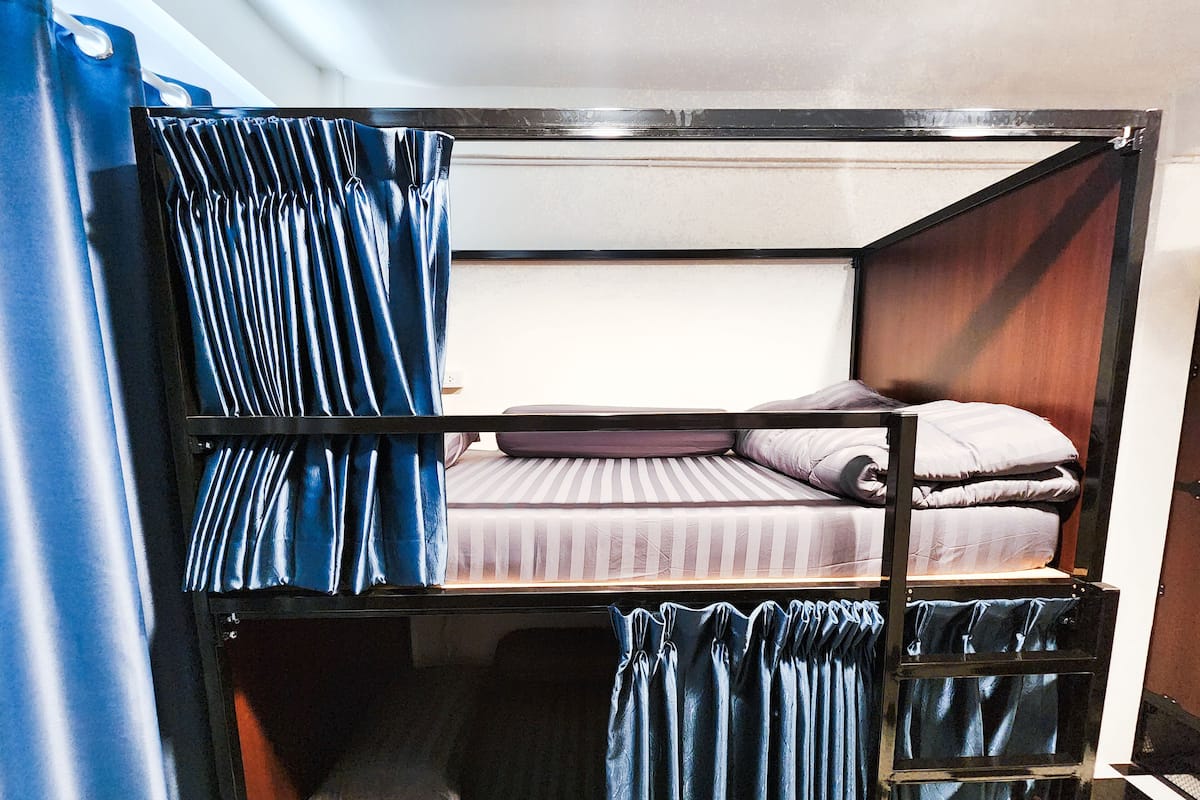A bunk bed room with curtains, a bed with striped bedding, and a wooden headboard.