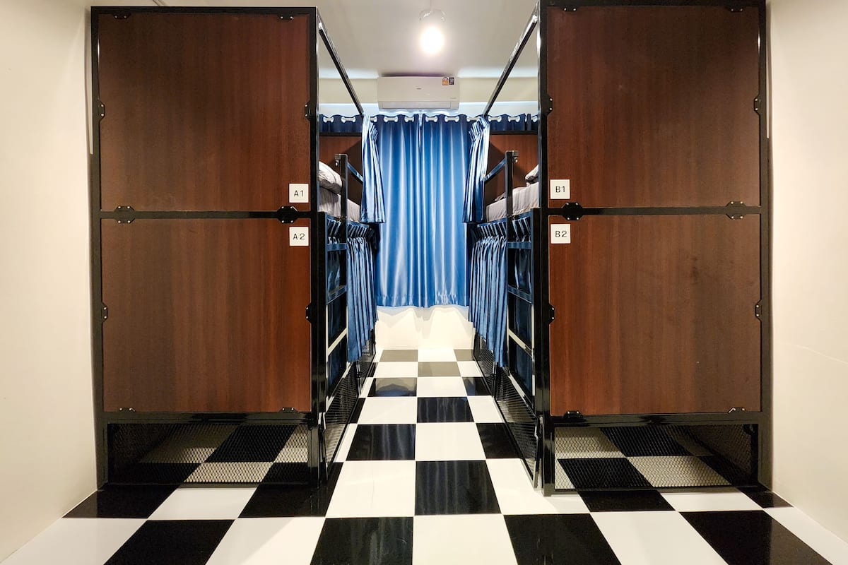 A corridor with bunk beds labeled A1, A2, B1, B2, leading to a room with a checkered floor and blue curtains.