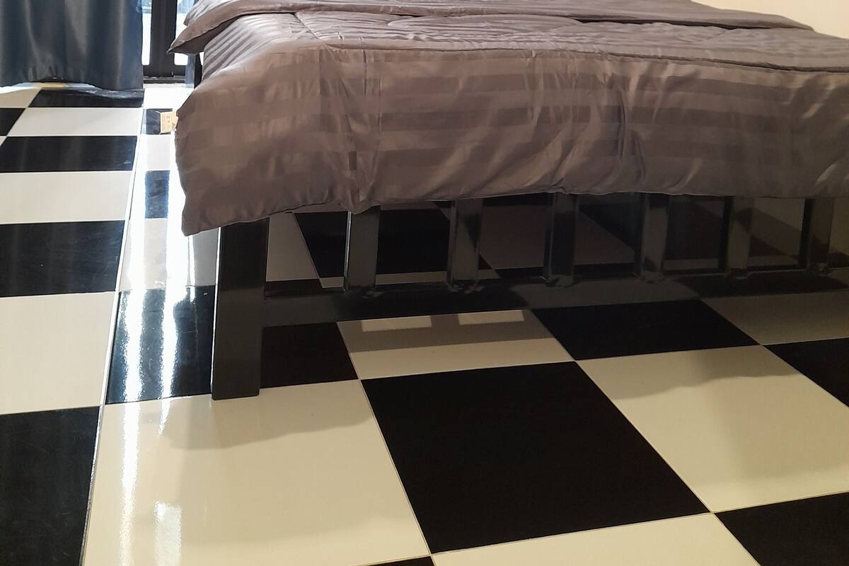 A room with a bed, a checkered floor, and a window with curtains.