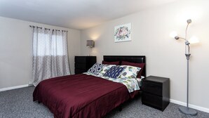 A bedroom with a bed, a nightstand, a floor lamp, a wall art piece, and a window with curtains. - Cozy Mountain Getaway: Perfect for Families, Groups and Pets (Tannersville)