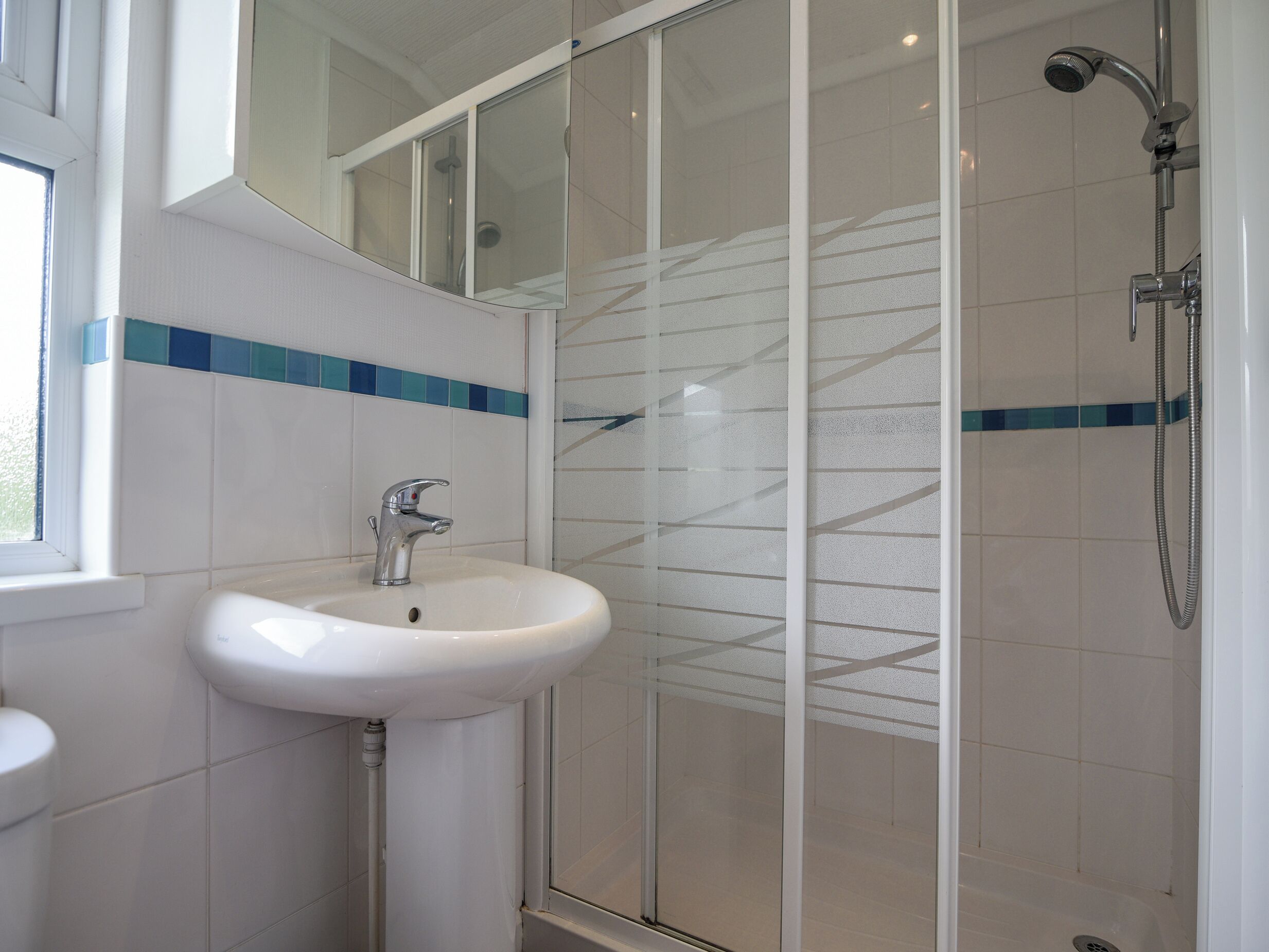 Un baño con lavamanos blanco, cabina de ducha con vidrio y ventana.