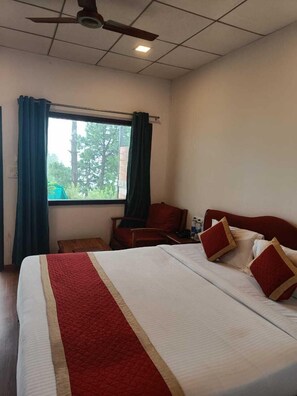 A hotel room with a bed, a desk, a chair, a window with curtains, and a ceiling fan. - Astre Vue Resort (Lansdowne)