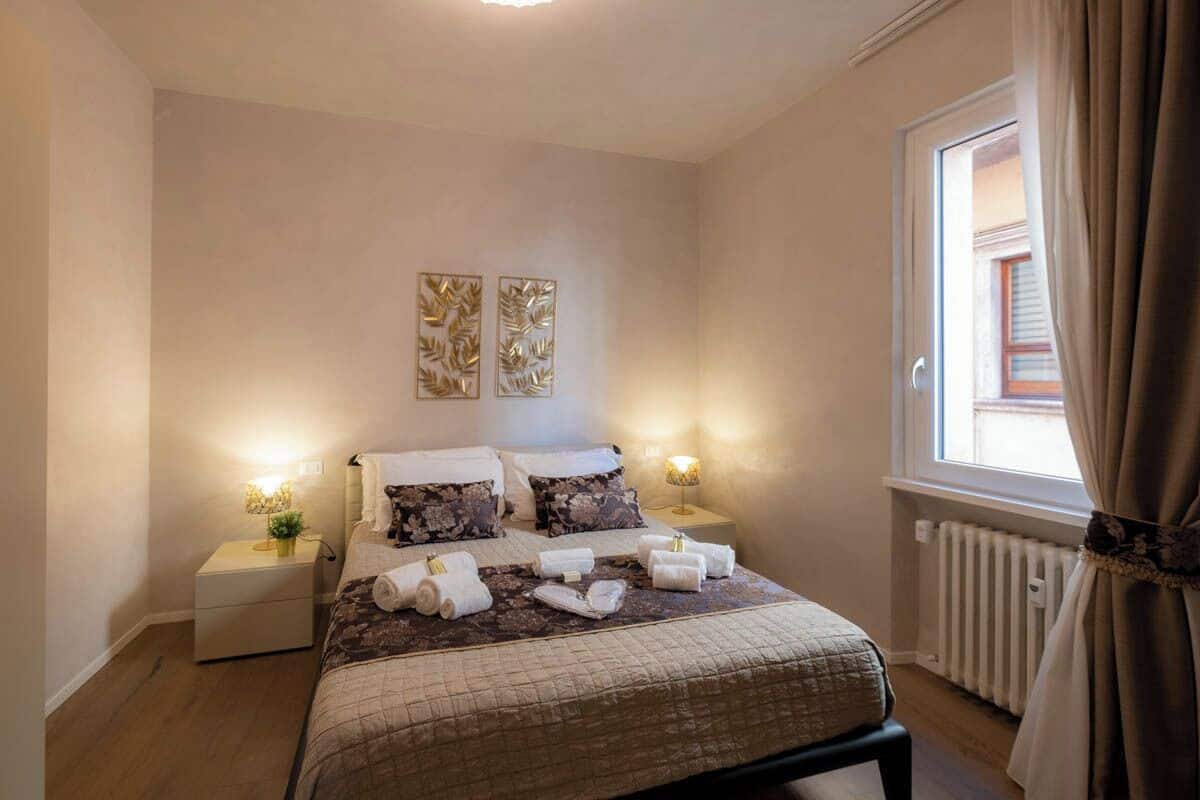 Ein ordentlich eingerichtetes Schlafzimmer mit einem Bett, zwei Nachttischen, einem Fenster mit Vorhängen und Wandbildern.