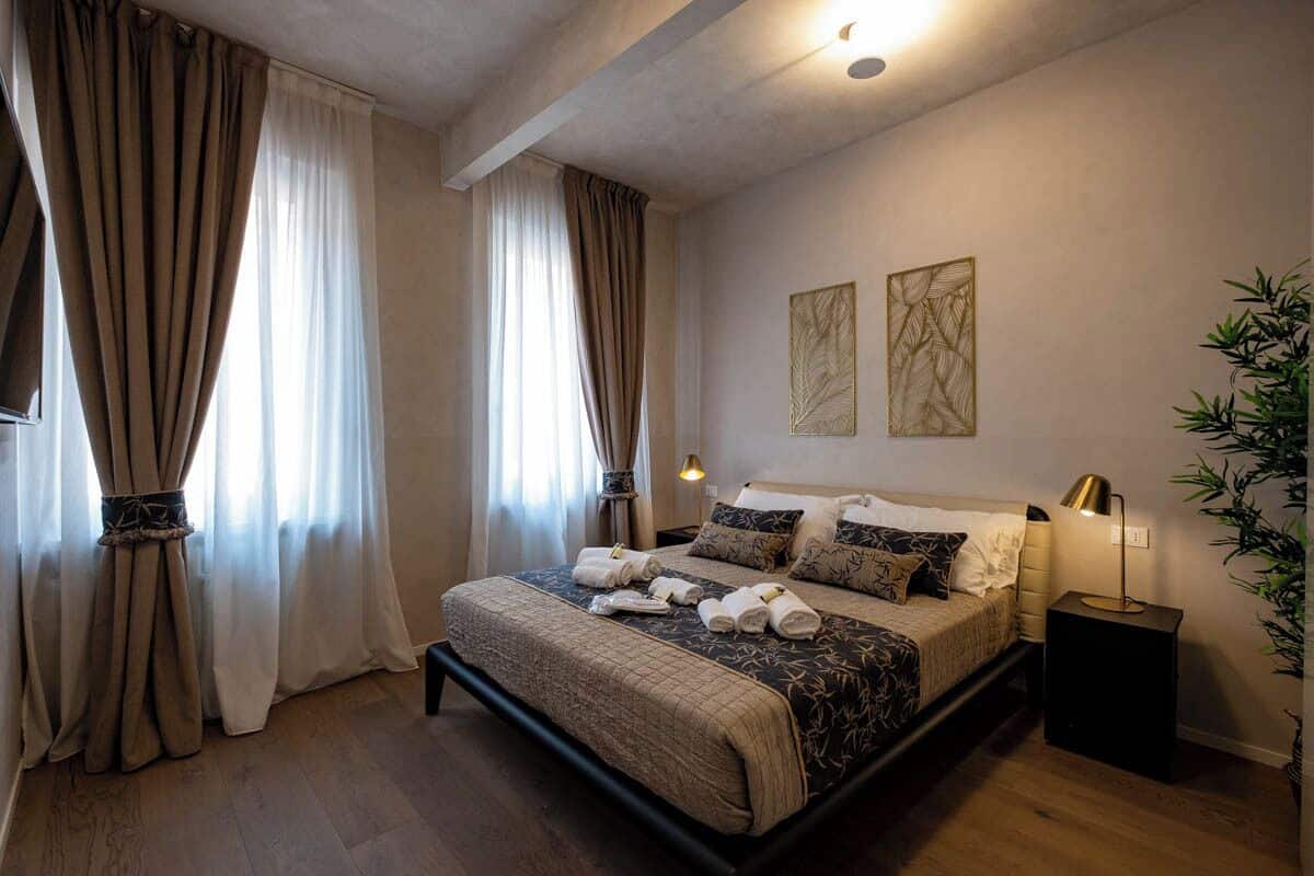 Ein Schlafzimmer mit Bett, Vorhängen, Wandbildern, einem Nachttisch und einer Pflanze.