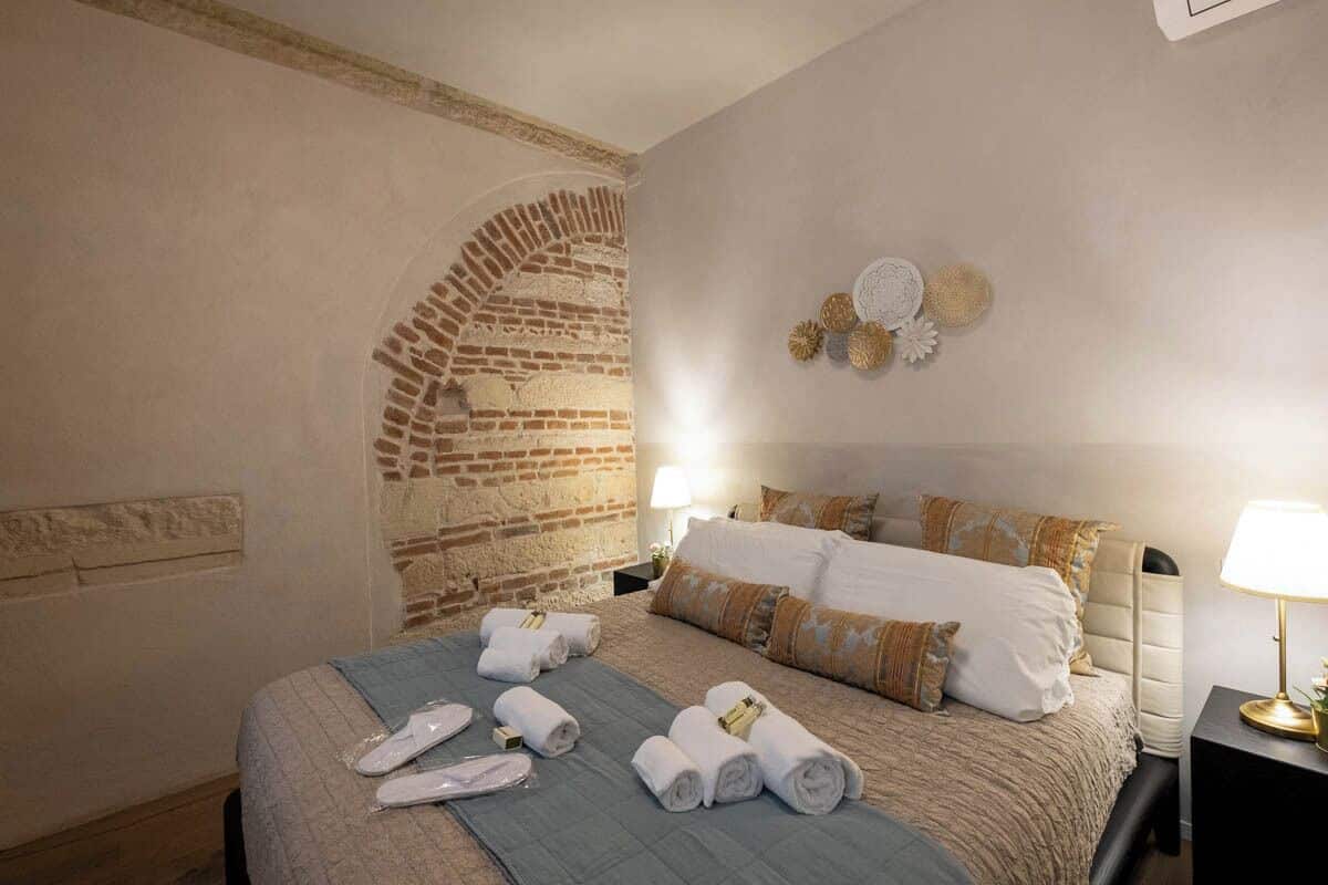 Ein Hotelzimmer mit einer Ziegelwand, einem Bett mit weißer und brauner Bettwäsche, einer blauen Tagesdecke und einem Nachttisch mit einer Lampe.