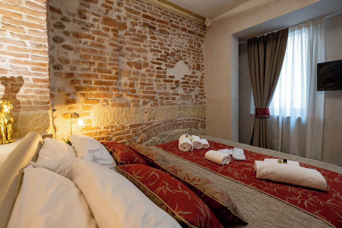 Een hotelkamer met een bakstenen muur, een bed met rode en witte beddengoed, en een raam met gordijnen.