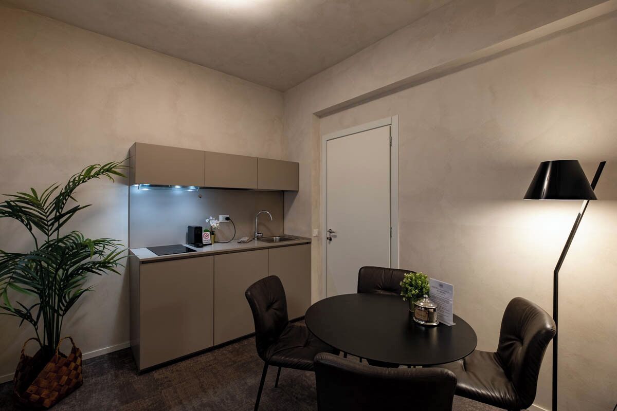 A compact kitchen with a sink, stove, and cabinets, a dining table with chairs, and a potted plant.