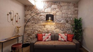 Ein gemütliches Zimmer mit Steinwand, einer Couch mit gemusterten Kissen, einem Schreibtisch mit Lampe und einer hohen Stehlampe.